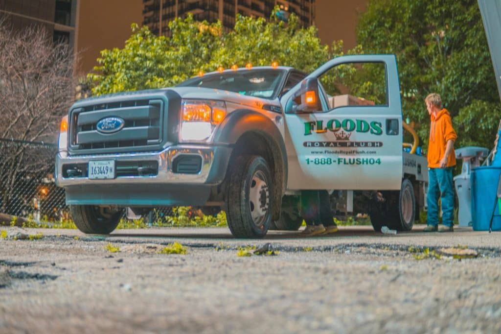 A pickup truck pulling up to construction site. The truck has "Floods Royal Flush" written on its open door.