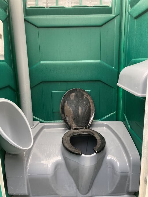The interior of a porta potty. There is a small toilet seat as well as a sink positioned next to the door.