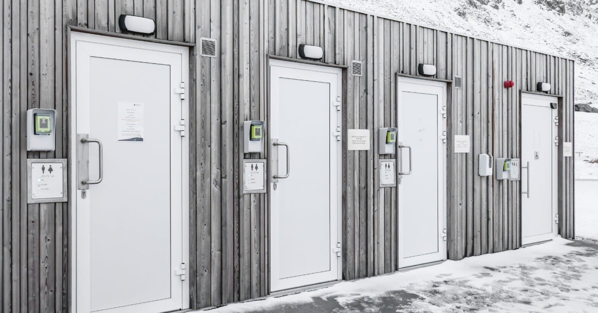 Portable toilets with multiple areas for people to use the restroom. There is snow on the ground outside the bathroom.