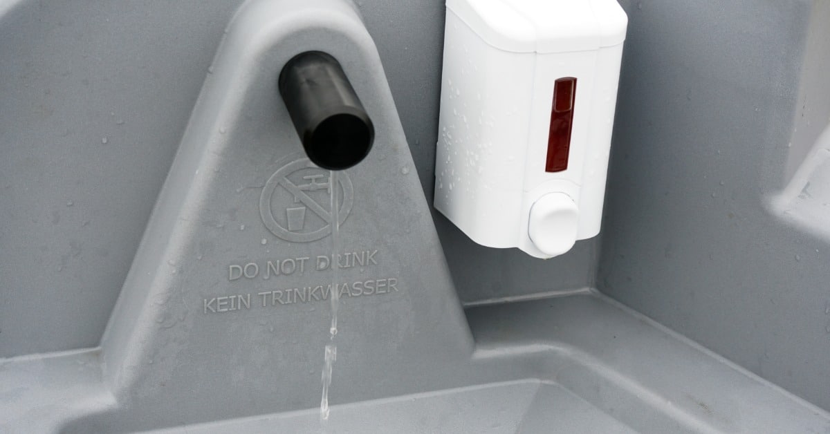 A close-up of a portable sink spout and soap dispenser with a do not drink water warning message.