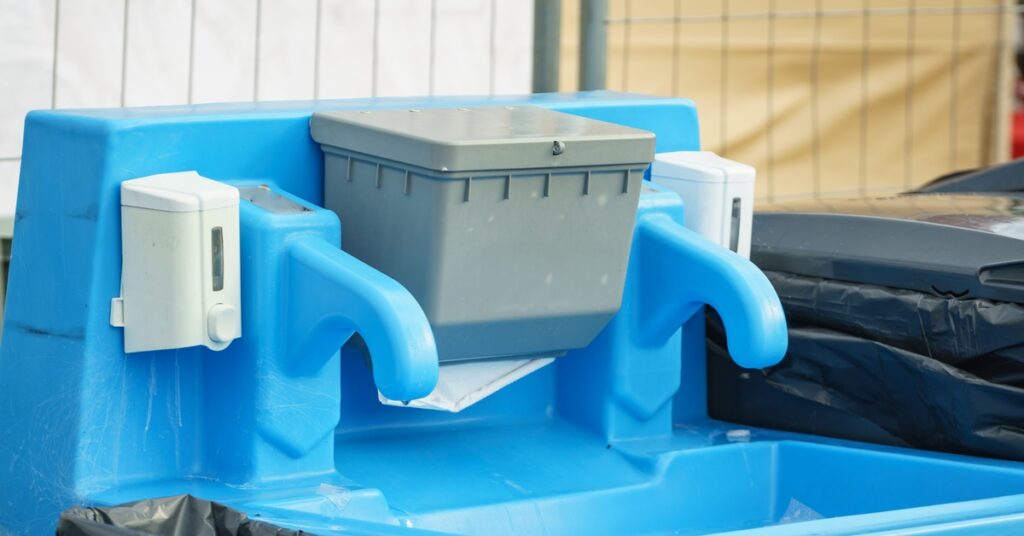 A blue outdoor handwashing station with two spouts, two soap dispensers, and a gray paper towel holder.