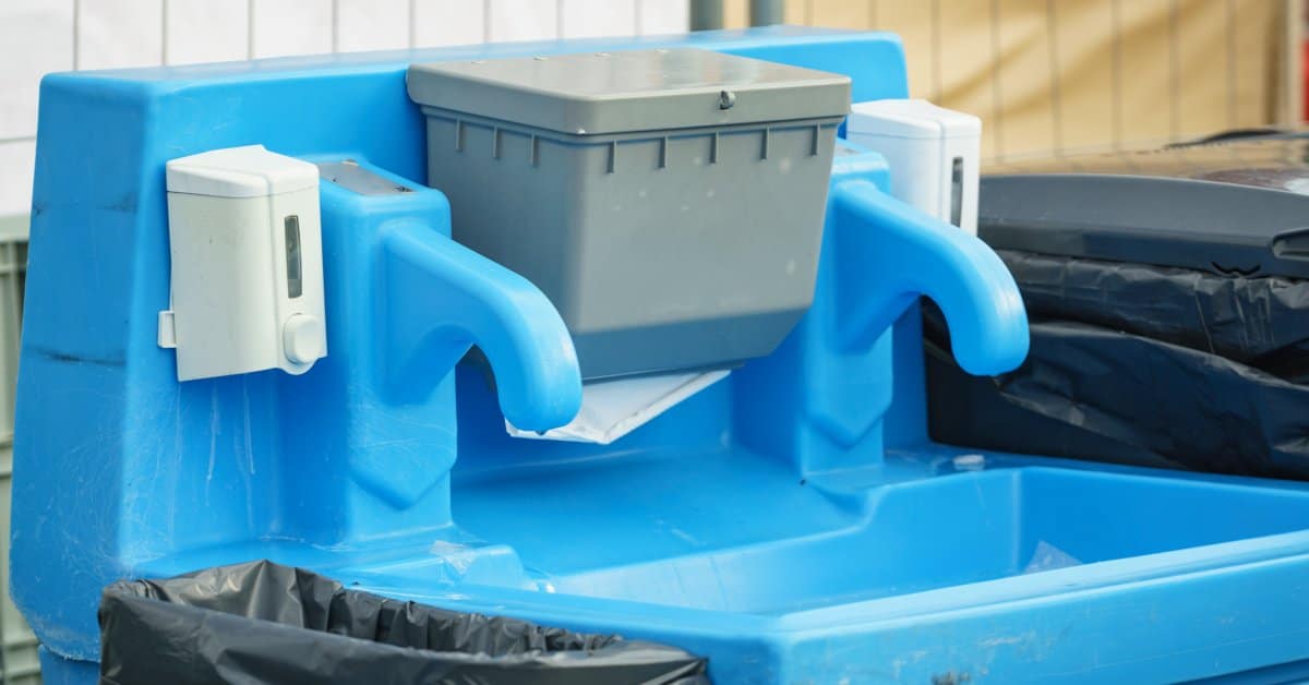 A close-up of a bright blue portable plastic sink with white soap dispensers outside and two trash cans on either side.