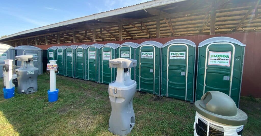 A lineup of portable bathroom stalls all placed next to one another outside. There are two handwashing stations nearby.