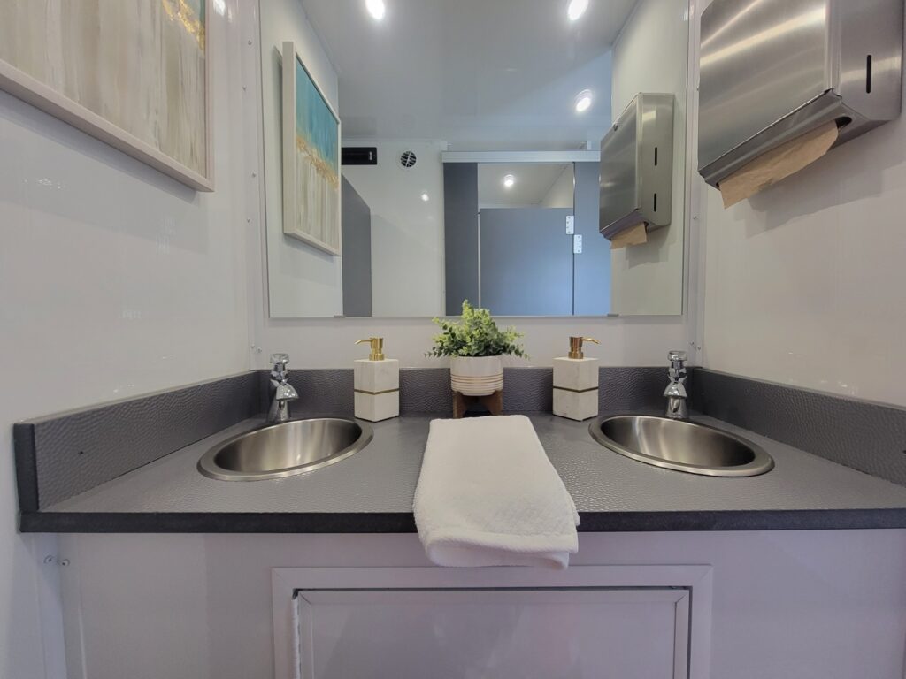 The inside of a portable bathroom trailer. There are two clean sinks situated next to each other for easy hand-washing.