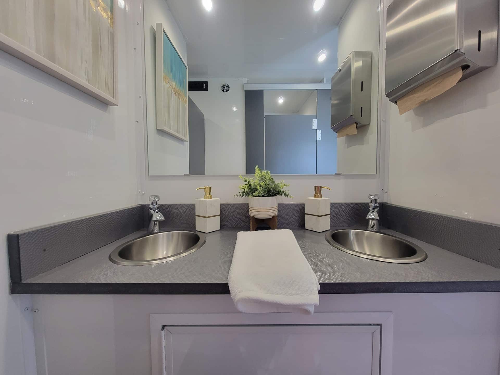 The inside of a portable bathroom trailer. There are two clean sinks situated next to each other for easy hand-washing.