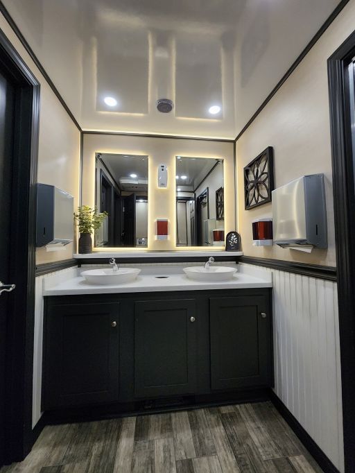 The interior of a luxury porta potty. There are two sinks side by side in front of two different mirrors.