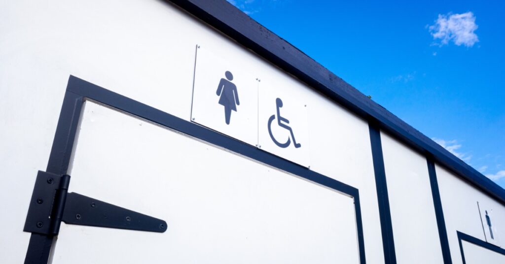 A portable toilet facility with markings above the doors. They also have a wheelchair-accessible space.