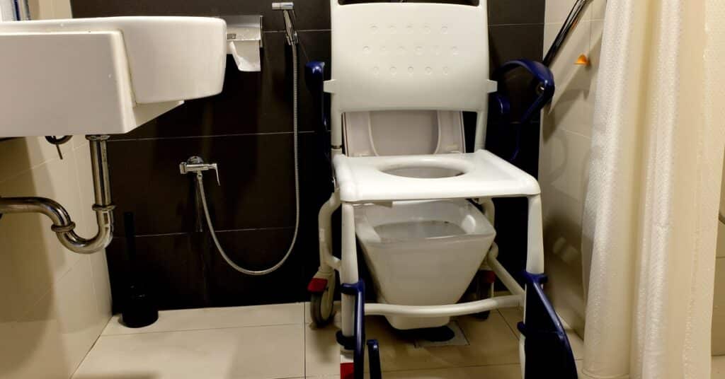 A mobile toilet seat placed over top of a toilet for use by handicapped individuals. A small sink is near the toilet as well.