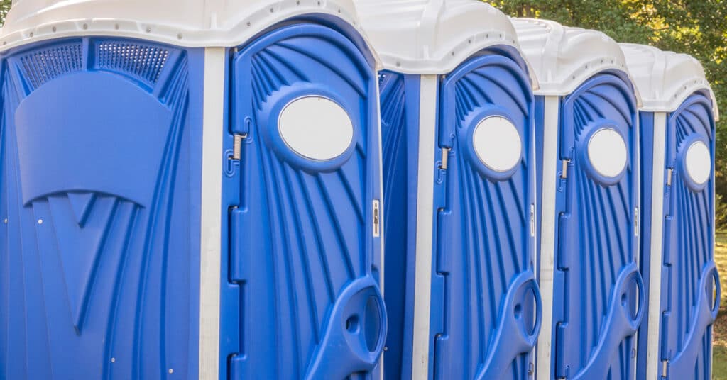 Four blue and white porta potties lined up together at an outdoor event. They're fully maintained and ready for use.