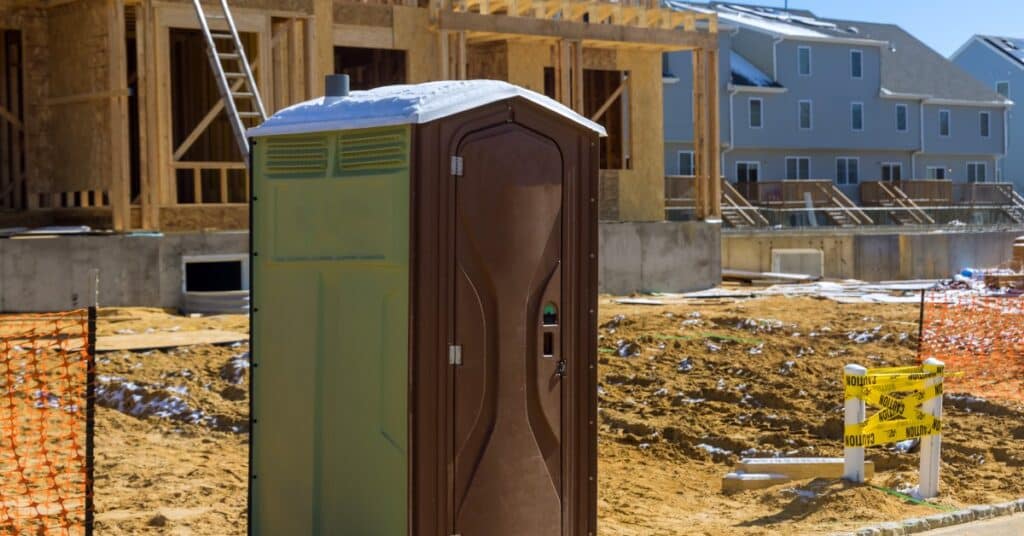 A green and black porta potty is on-site at a new residential construction project that provides accessible restrooms.