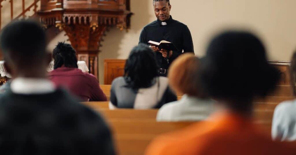 A young Black pastor reads from the Bible to the congregation seated in pews during a church service.