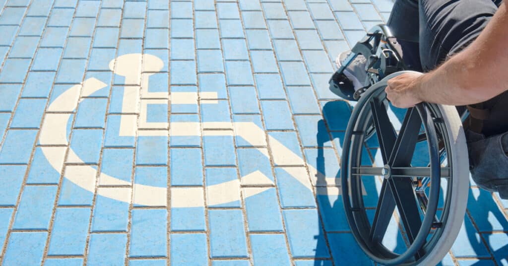 A wheelchair user navigates an accessible blue tiled pathway with a handicap symbol, demonstrating ADA compliance.