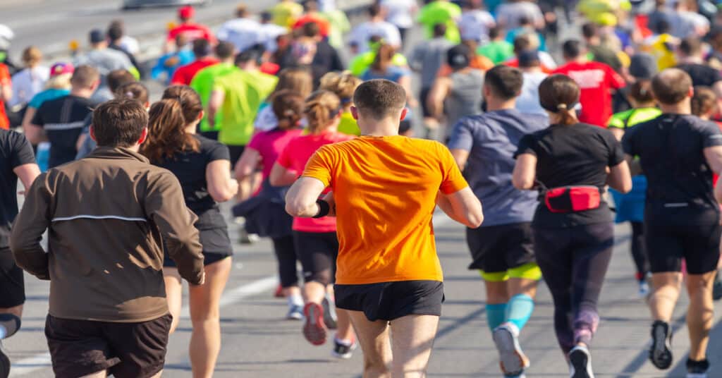 Runners in colorful athletic gear move together along a city street during a marathon, showing crowd flow and race day energy.