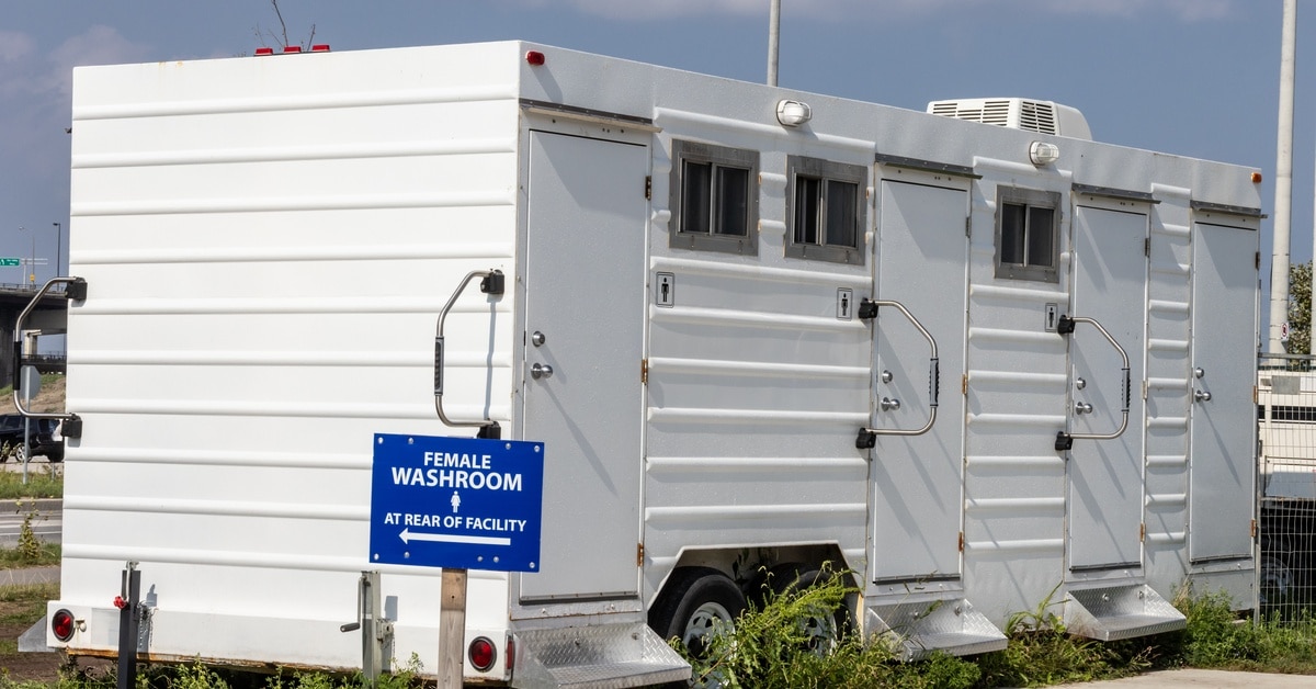 A white multi-stall restroom trailer with a female washroom sign parked outdoors at a construction or event site.