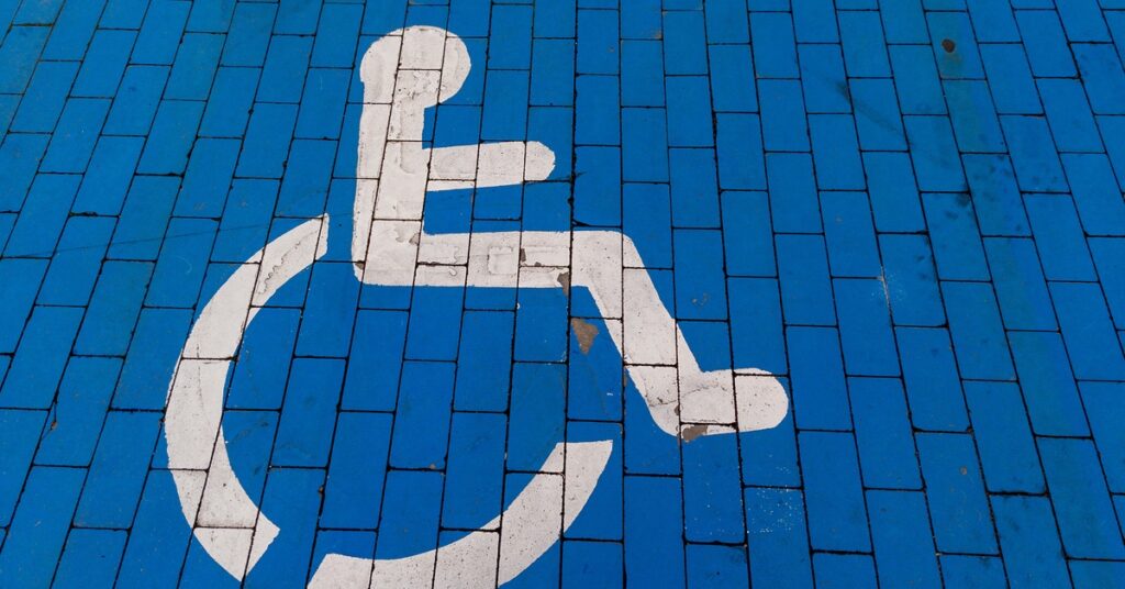 A white international wheelchair accessibility symbol painted on blue brick pavement indicating a handicapped accessible zone.